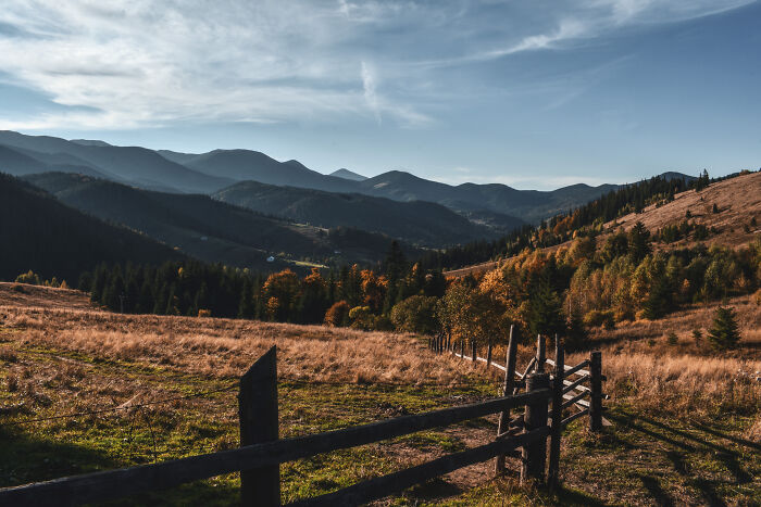 Ukrainian Carpathians landscape with rolling hills, autumn trees, and a rustic wooden fence under a cloudy sky.