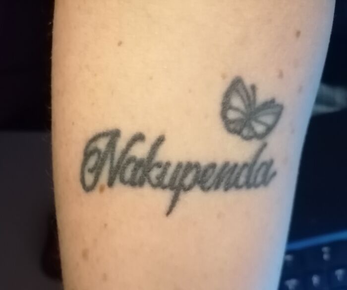 Tattoo of the word "Nakupenda" with a butterfly design on skin.