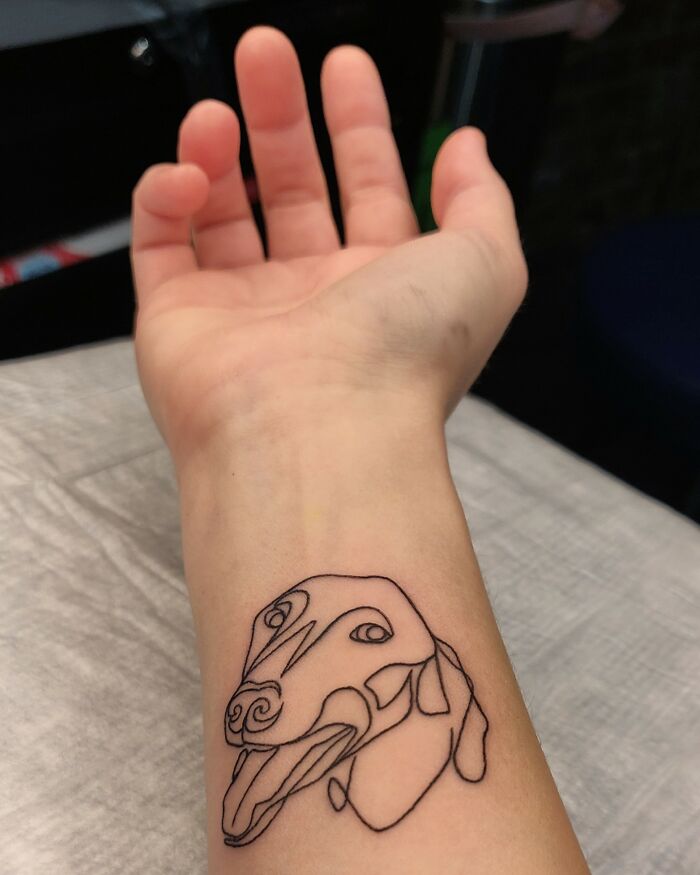 Tattoo of an abstract dog outline on a person's wrist.