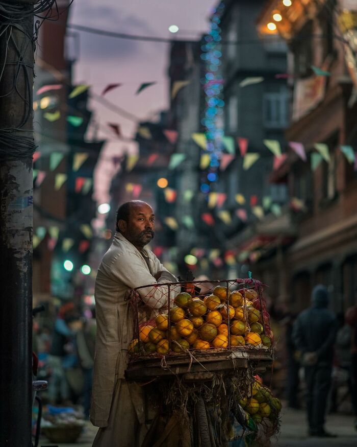 Man selling fruit in a narrow street at dusk, capturing the quiet side of city life in South Asia.