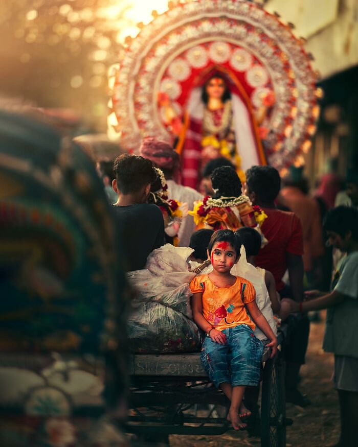 Young child with face paint sitting on a decorated cart in narrow South Asian street capturing quiet city life moments.