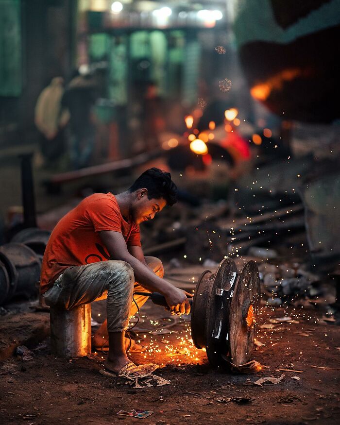 Young man working with sparks in a quiet narrow street, capturing the calm side of city life in South Asia.