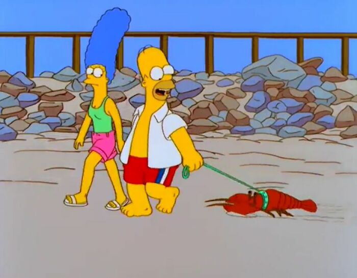 Homer and Marge Simpson walking on the beach with Homer holding a lobster on a leash in The Simpsons show.