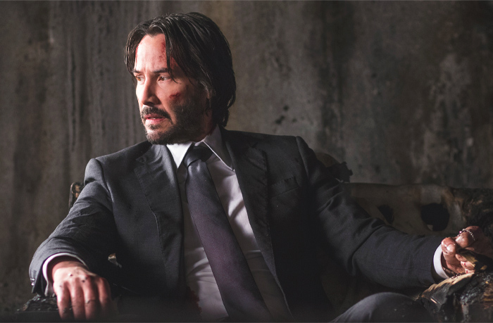 Keanu Reeves with scratches on his face sitting in an armchair