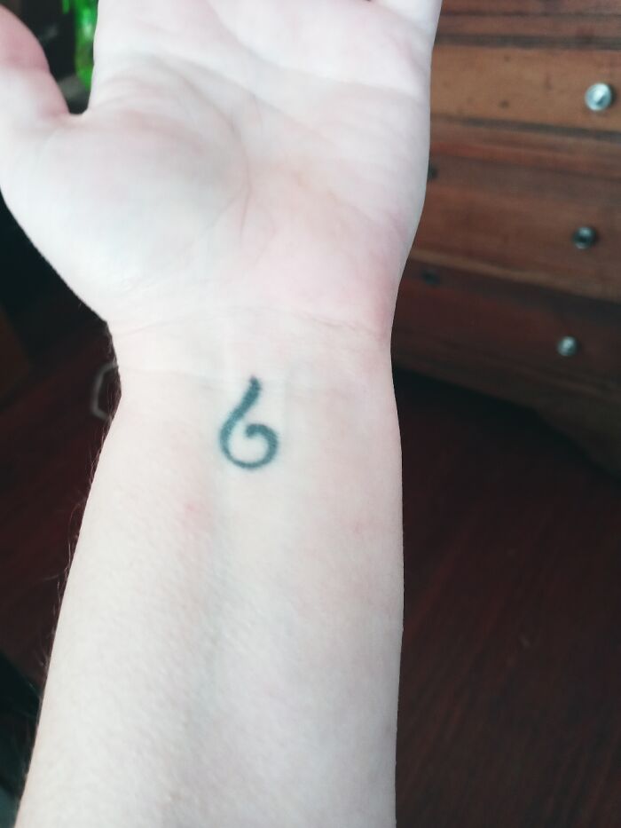 Close-up of a wrist with a small tattoo of the number six.