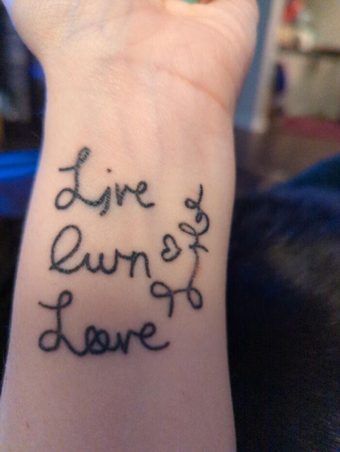 Tattoo on forearm with script text "Live, Laugh, Love" in elegant cursive style.