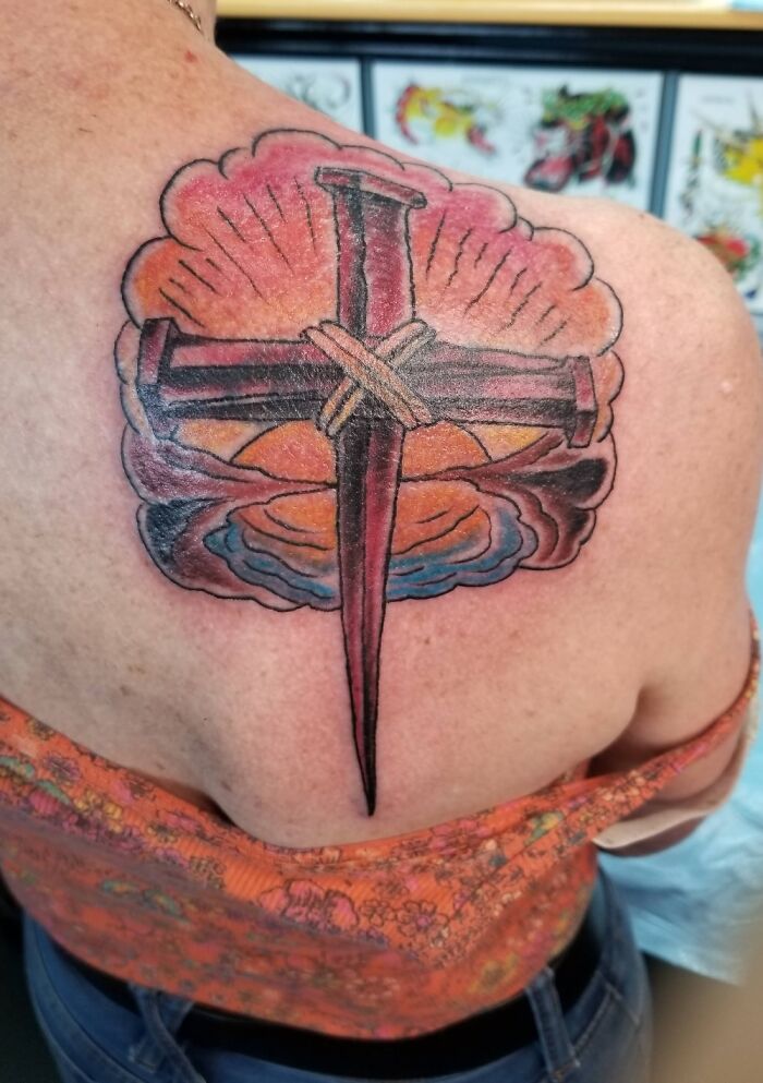 A detailed cross tattoo on a person's back, featuring vibrant colors and intricate design elements.