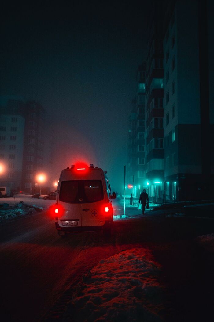 Ambulance with red lights on at night near buildings, evoking stories of people who came back to life experiences.