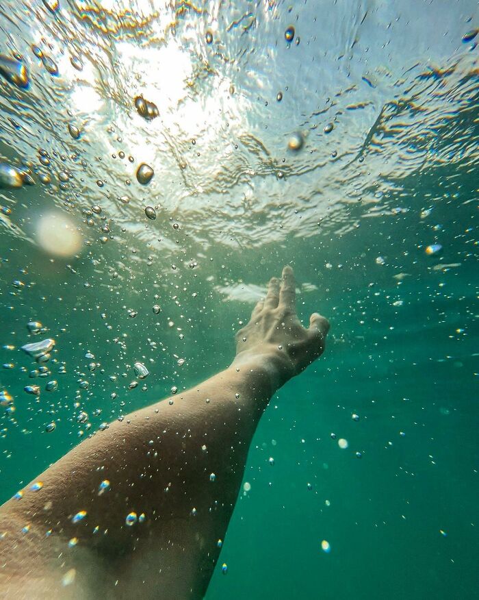 Underwater view of an arm reaching toward the surface with bubbles, illustrating people who came back to life experiences.