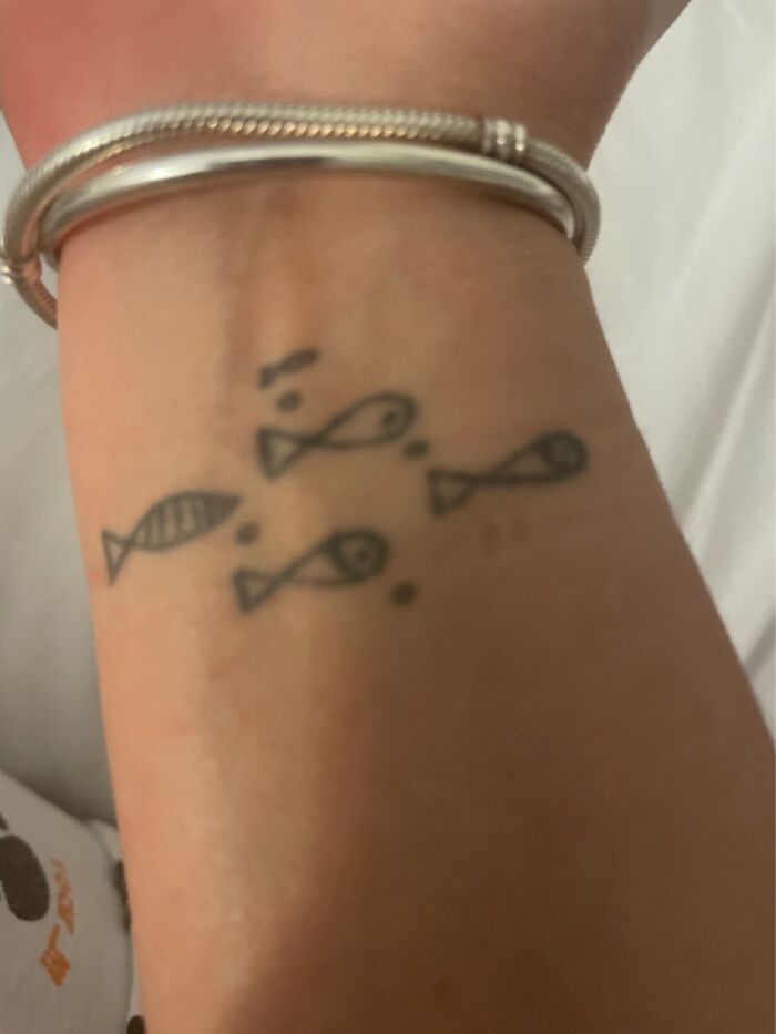 Wrist with small fish tattoos and silver bracelets, showcasing tattoos.