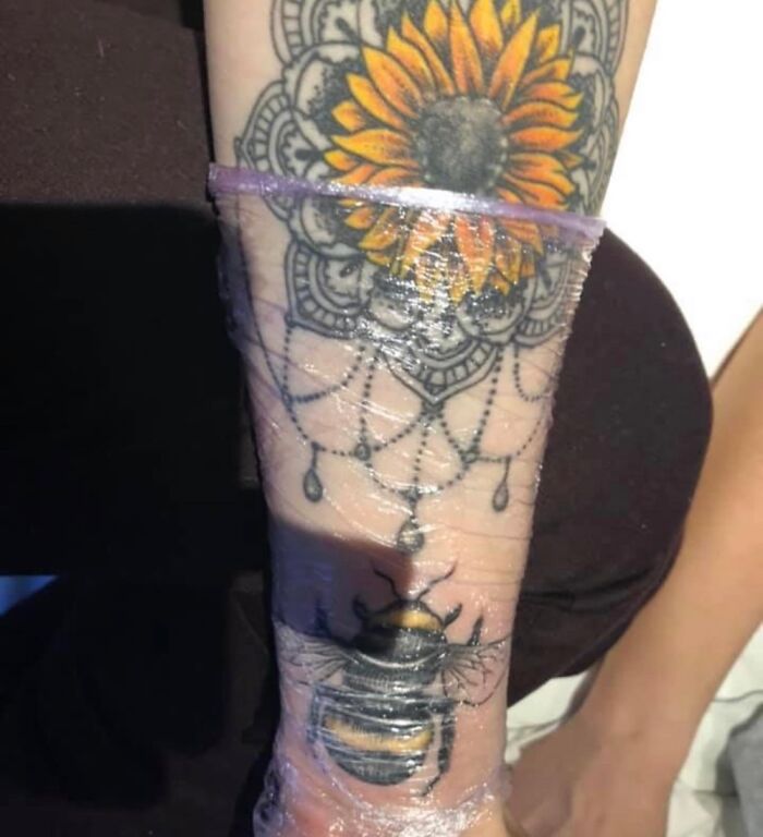 Sunflower and bee tattoo on arm, featuring intricate mandala design, covered in protective wrap.