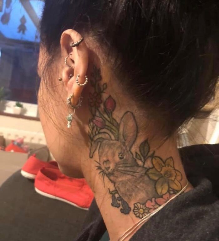 Woman with ear piercings and a colorful rabbit tattoo on her neck, featuring flowers.