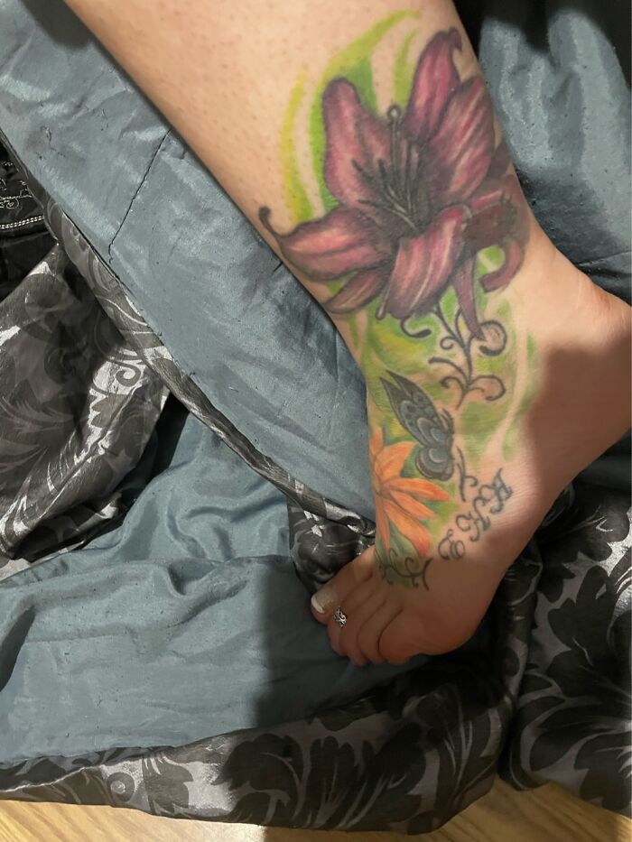 Colorful floral tattoo on a foot, featuring a pink flower with green and orange accents.