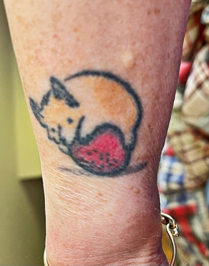 Cartoon mouse tattoo holding a red strawberry on an arm, showcasing unique body art.