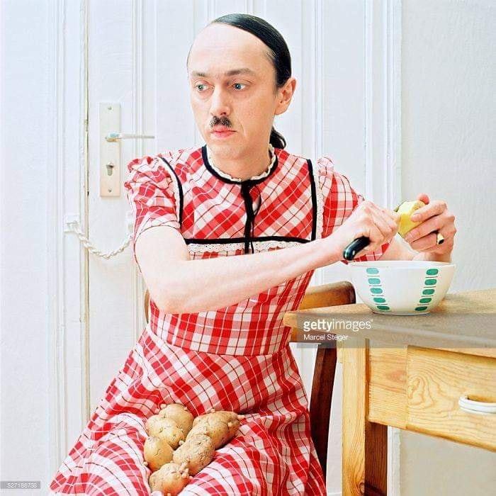 A person peeling a fruit in a red checkered dress with potatoes on their lap; a weird stock image.