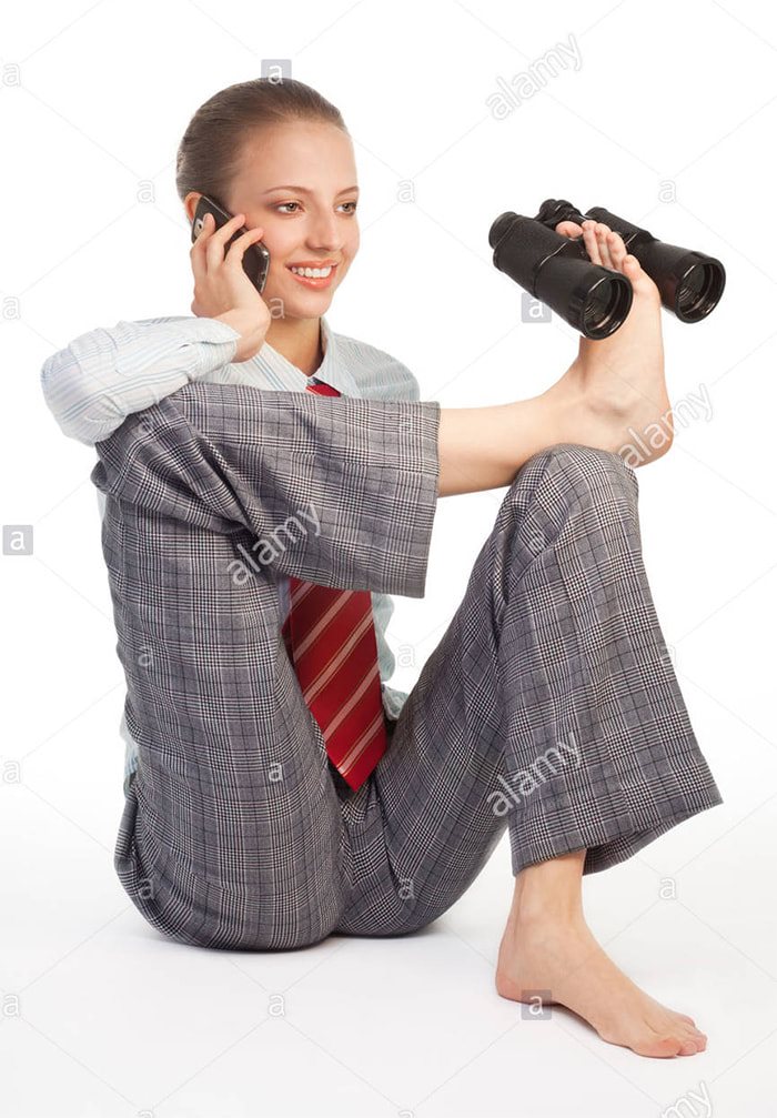 A woman in a plaid suit holds binoculars with her foot while talking on the phone, exemplifying weird stock images.