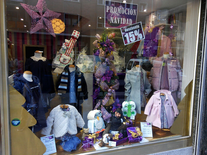 Children's clothing store window display with winter coats, festive decorations, and discount signs highlighting big scams.