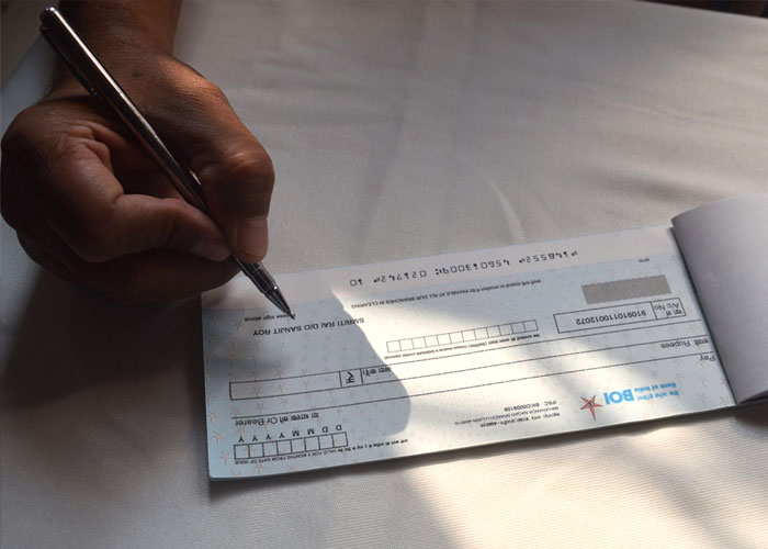 Person writing a check with a pen on a white surface illustrating delusional and out-of-touch statements concept.