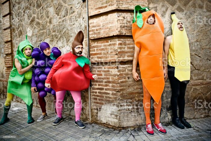 People in fruit and vegetable costumes standing by a brick wall, showcasing one of the weirdest stock images.