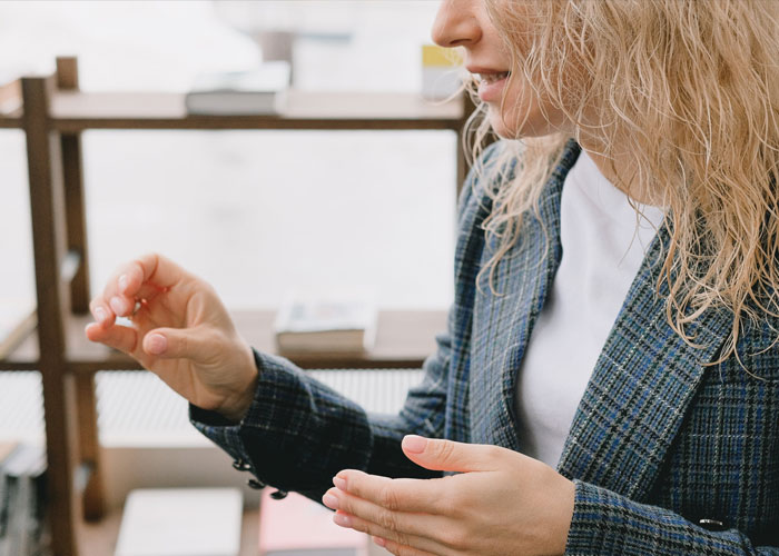 Woman in a plaid blazer gesturing while speaking, illustrating delusional and out-of-touch things people say.
