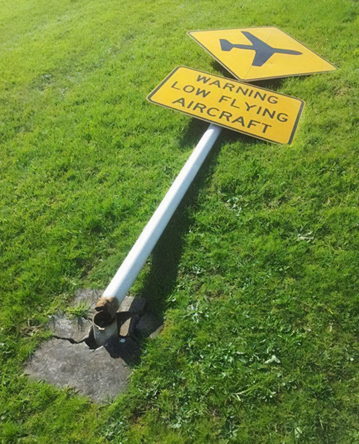 Yellow warning sign for low flying aircraft fallen on grass, an example of hilarious and absurd signs spotted by people.