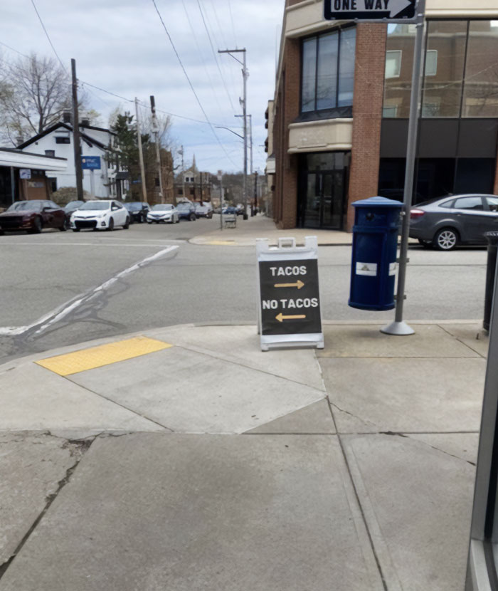 Hilarious and absurd sign on a sidewalk with arrows pointing right for tacos and left for no tacos.