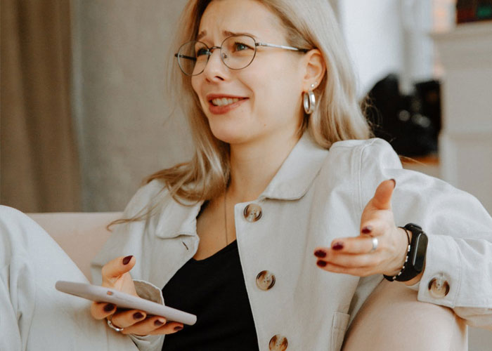 Young woman with glasses holding phone, expressing disbelief at delusional and out-of-touch things people say.