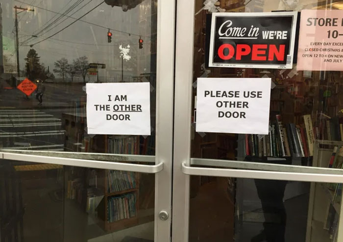 Two glass doors with funny and absurd signs saying I am the other door and Please use other door visible.