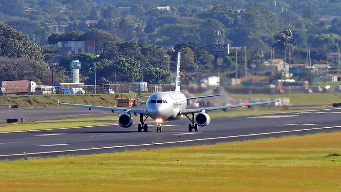 Airplane taxiing on runway surrounded by green fields and distant trees illustrating big scams discussed in online group.