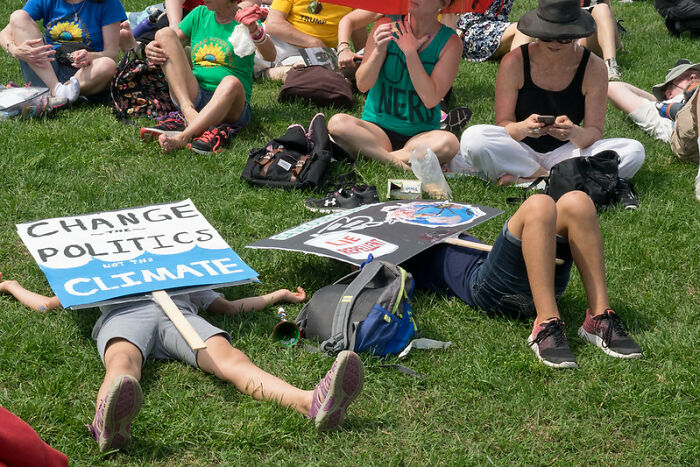 Protesters sitting and lying on grass holding signs about climate and politics, illustrating common big scams topics.