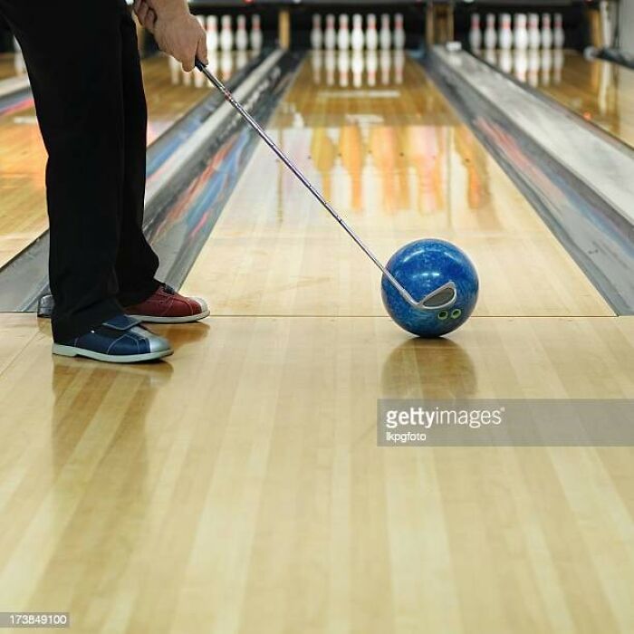 Man using a golf club to position a bowling ball on a lane, showcasing a weird stock image scenario.