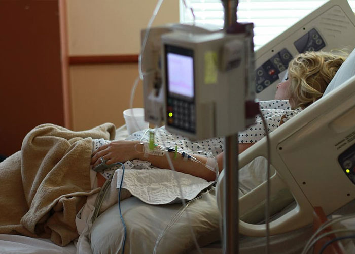Patient lying in a hospital bed receiving IV treatment, illustrating delusional and out-of-touch situations heard in conversations.