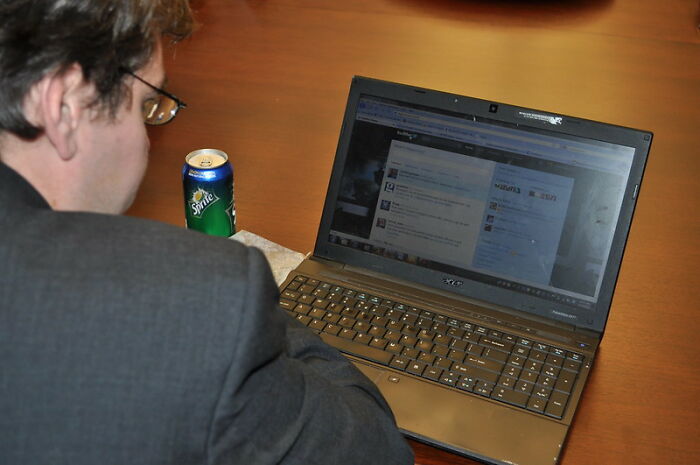 Person browsing an online group discussing big scams on a laptop with a can of Sprite on the table.