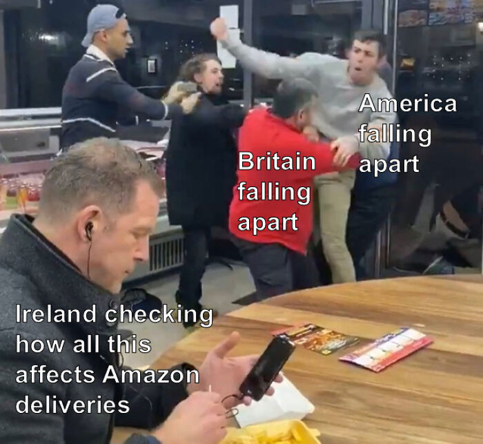Man focused on phone ignoring a chaotic fight labeled Britain and America falling apart, highlighting Irish humor online posts.