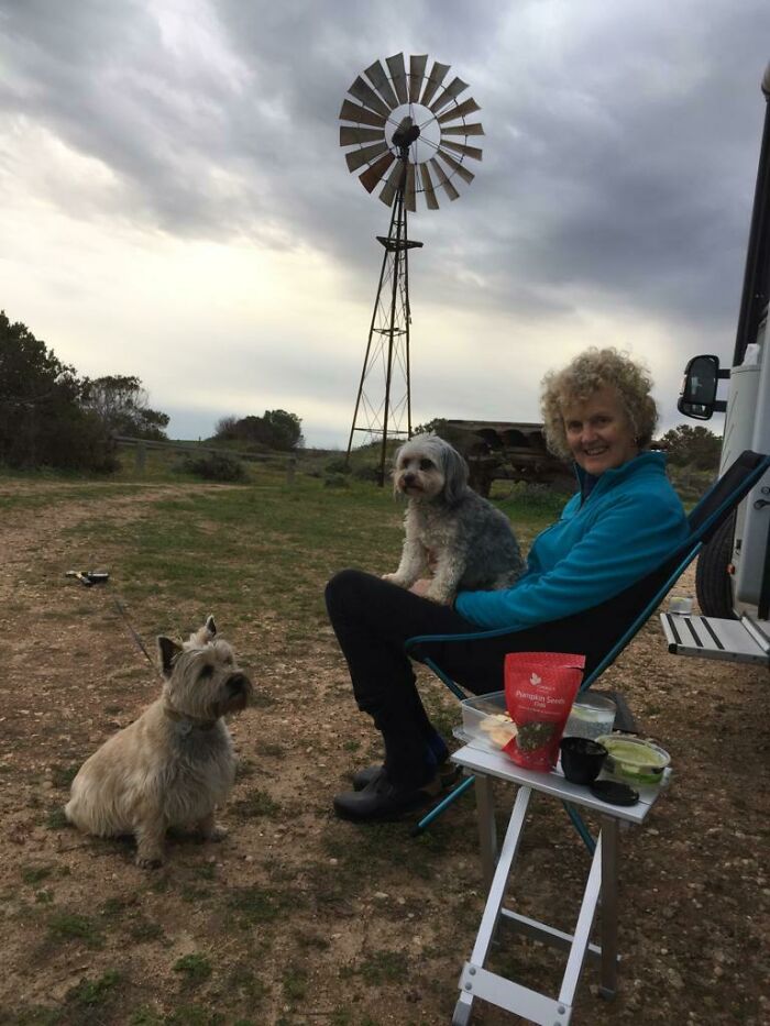 Woman sitting outdoors with two dogs near a windmill, showcasing one of the best mothers-in-law in a natural setting.