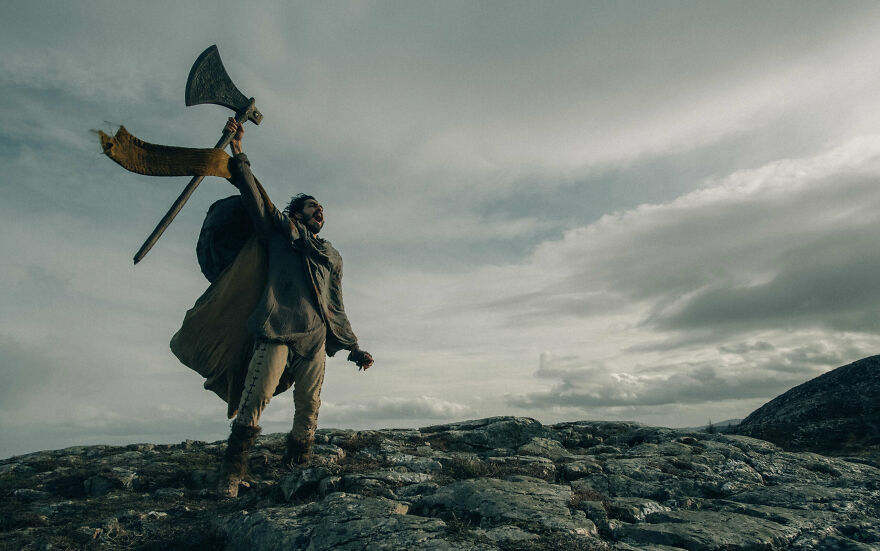 A man standing on the rocks with a large axe lifted up in his right hand