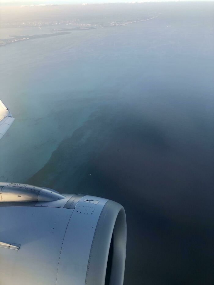 Plane wing and engine flying over dark deep waters, capturing a view that may trigger thalassophobia and fear of deep waters.
