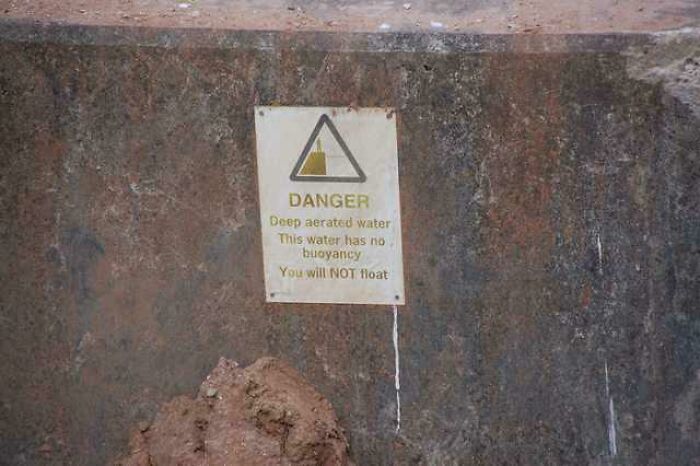 Warning sign on a concrete wall about deep aerated water with no buoyancy, triggering thalassophobia fears.