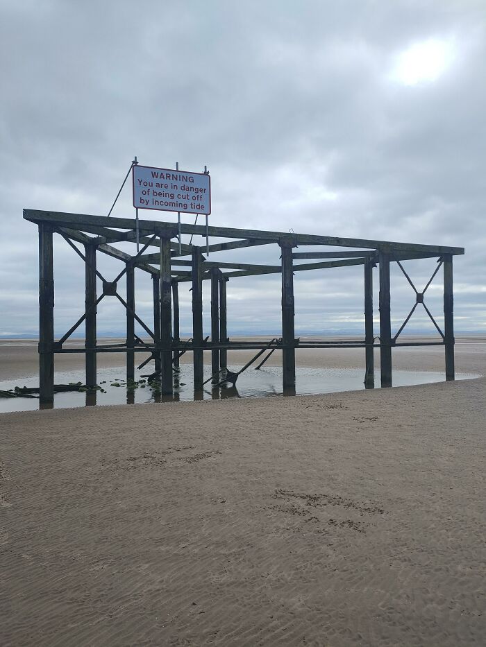 Old wooden pier structure on a sandy beach under cloudy sky, evoking thalassophobia and fear of deep waters.
