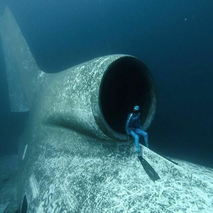 Diver sitting at the entrance of a large underwater structure, illustrating thalassophobia and deep waters fear.