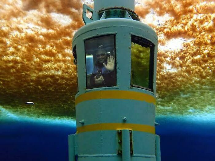 Man inside a submarine window submerged underwater, surrounded by deep waters triggering thalassophobia fears.