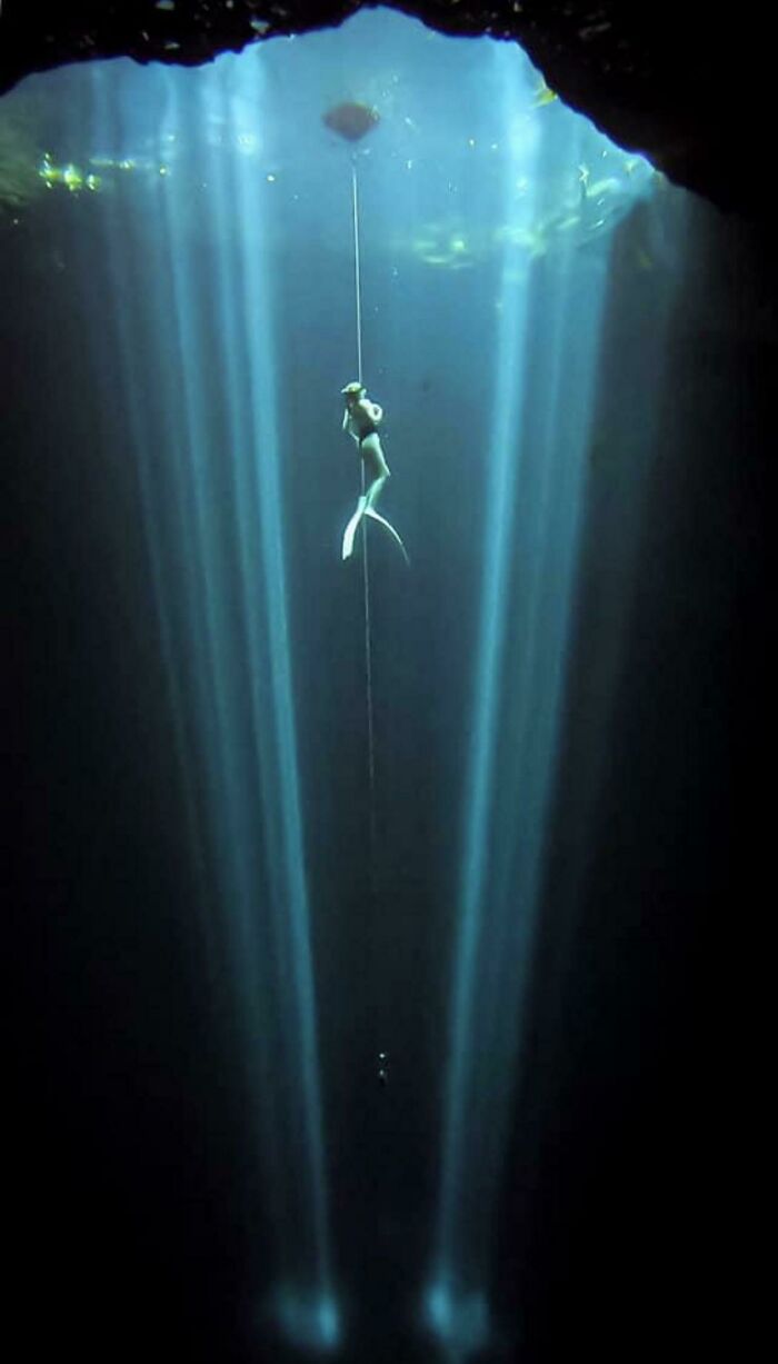 Freediver descending into deep waters with light beams penetrating the dark ocean, triggering thalassophobia fears.