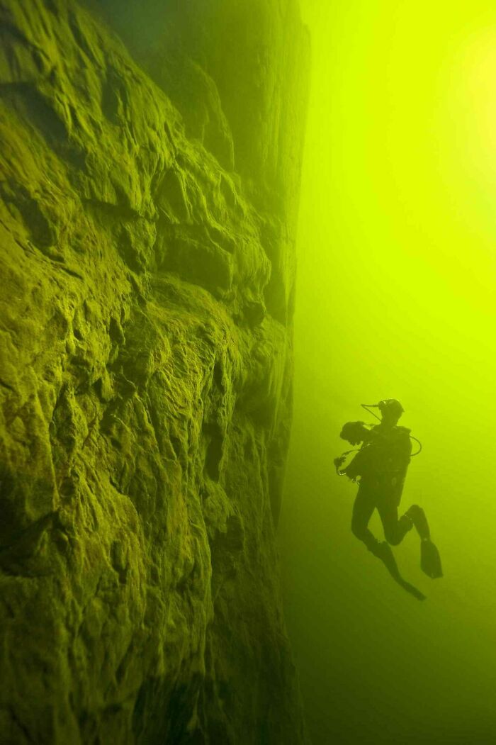 Scuba diver near a towering underwater rock wall, surrounded by murky water triggering thalassophobia fears.