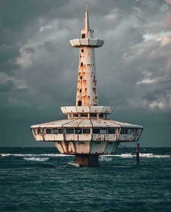 Rust-covered abandoned structure rising from deep dark waters under a cloudy sky, evoking thalassophobia in the ocean.