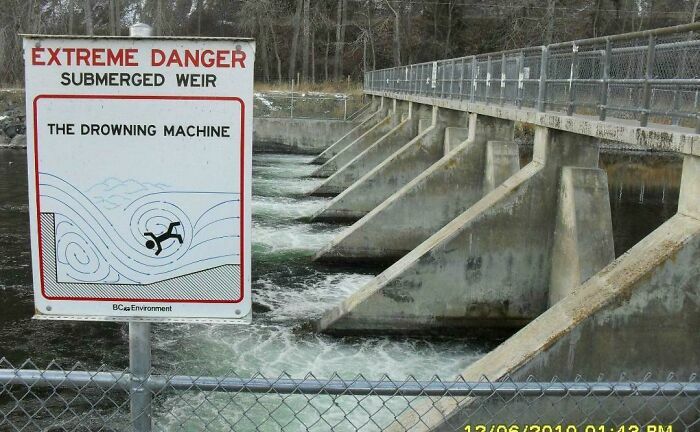Warning sign at a submerged weir above turbulent water, illustrating dangers linked to thalassophobia and deep water fears.