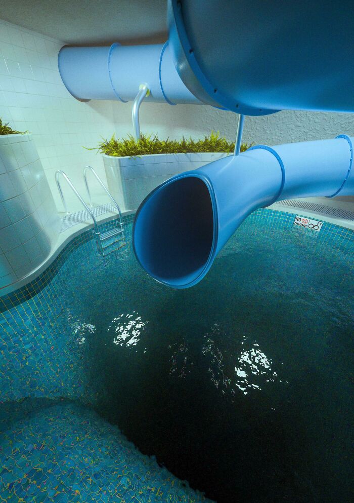 Blue water slide empties into a deep, dark swimming pool, capturing feelings related to thalassophobia and fear of deep waters.