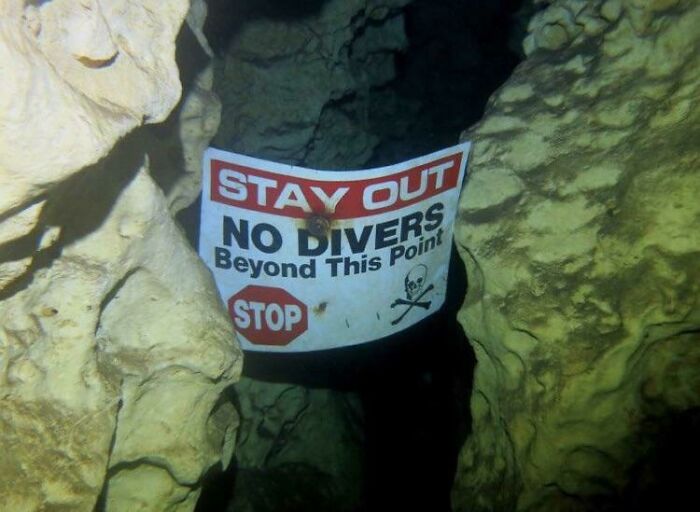Warning sign in underwater cave reading stay out no divers beyond this point, triggering thalassophobia fear of deep waters.