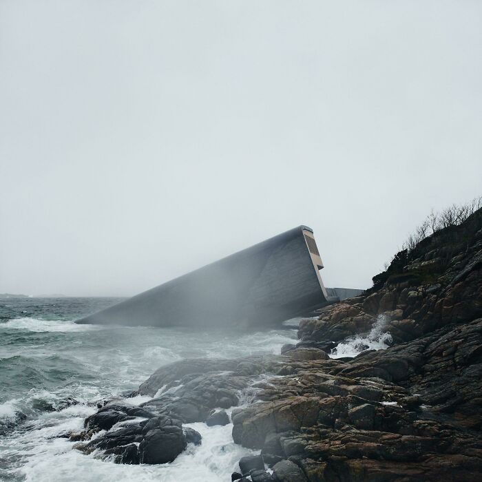 Stormy sea crashes against rocky shore with a mysterious structure partially submerged, evoking thalassophobia and deep water fear.