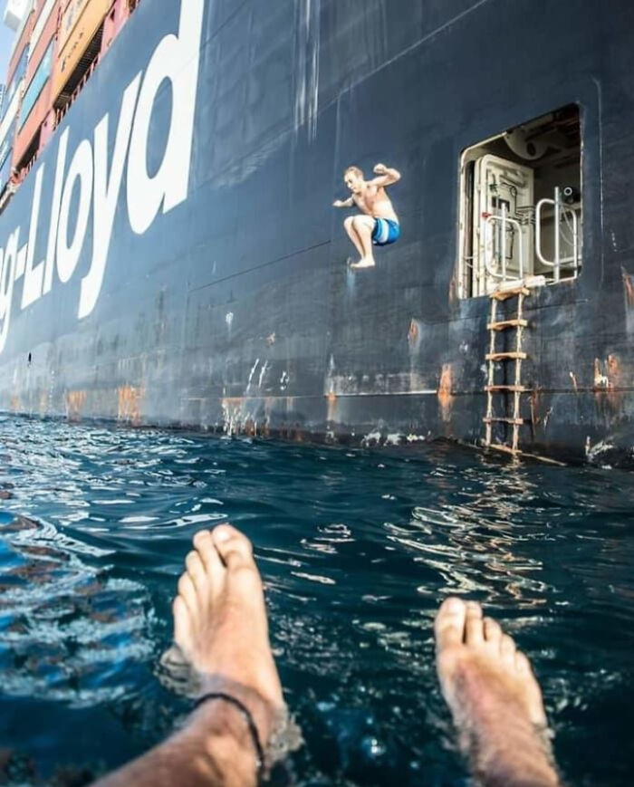 Person jumping off a large ship into deep waters with another person’s feet visible in the foreground, triggering thalassophobia.