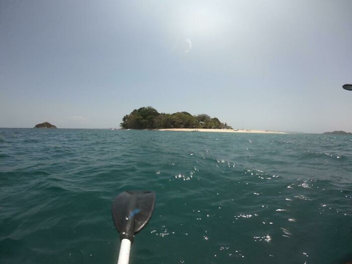 View from a kayak paddle on open ocean water with a small island in the distance, capturing deep waters and thalassophobia triggers.